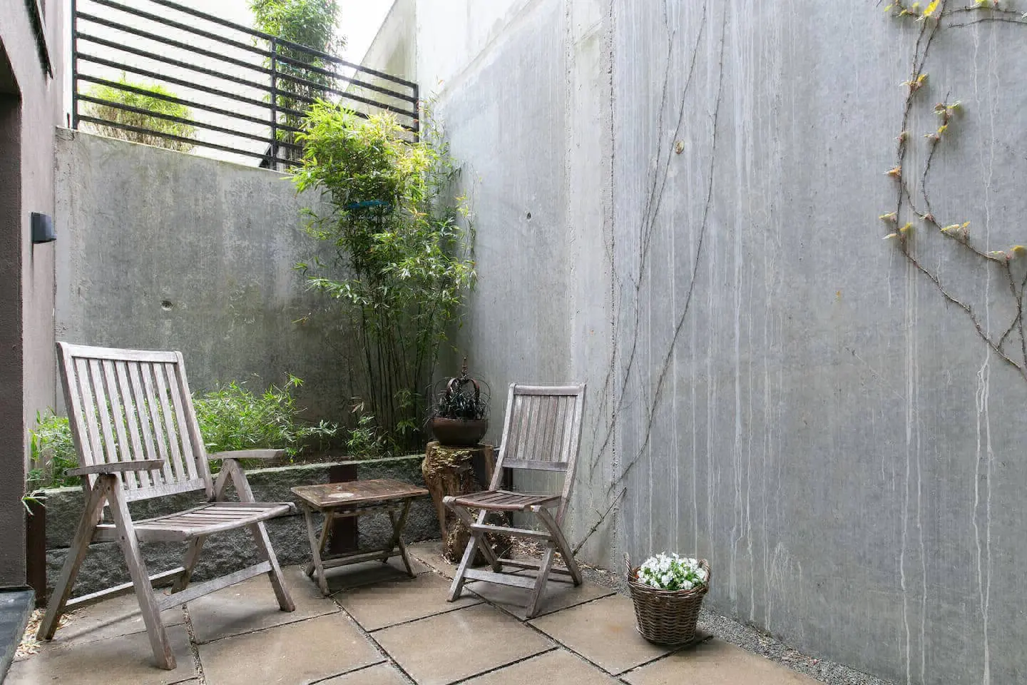 Betonhof mit Gartenstuhl, Blumenkorb und Pflanzen auf Steinplatten