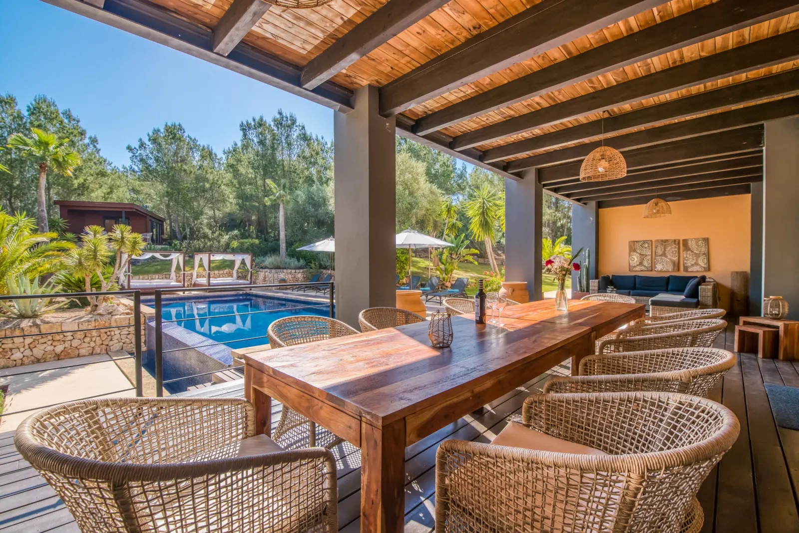 Überdachte Terrasse mit langem Holztisch, Rattanstühlen und Blick zum Pool