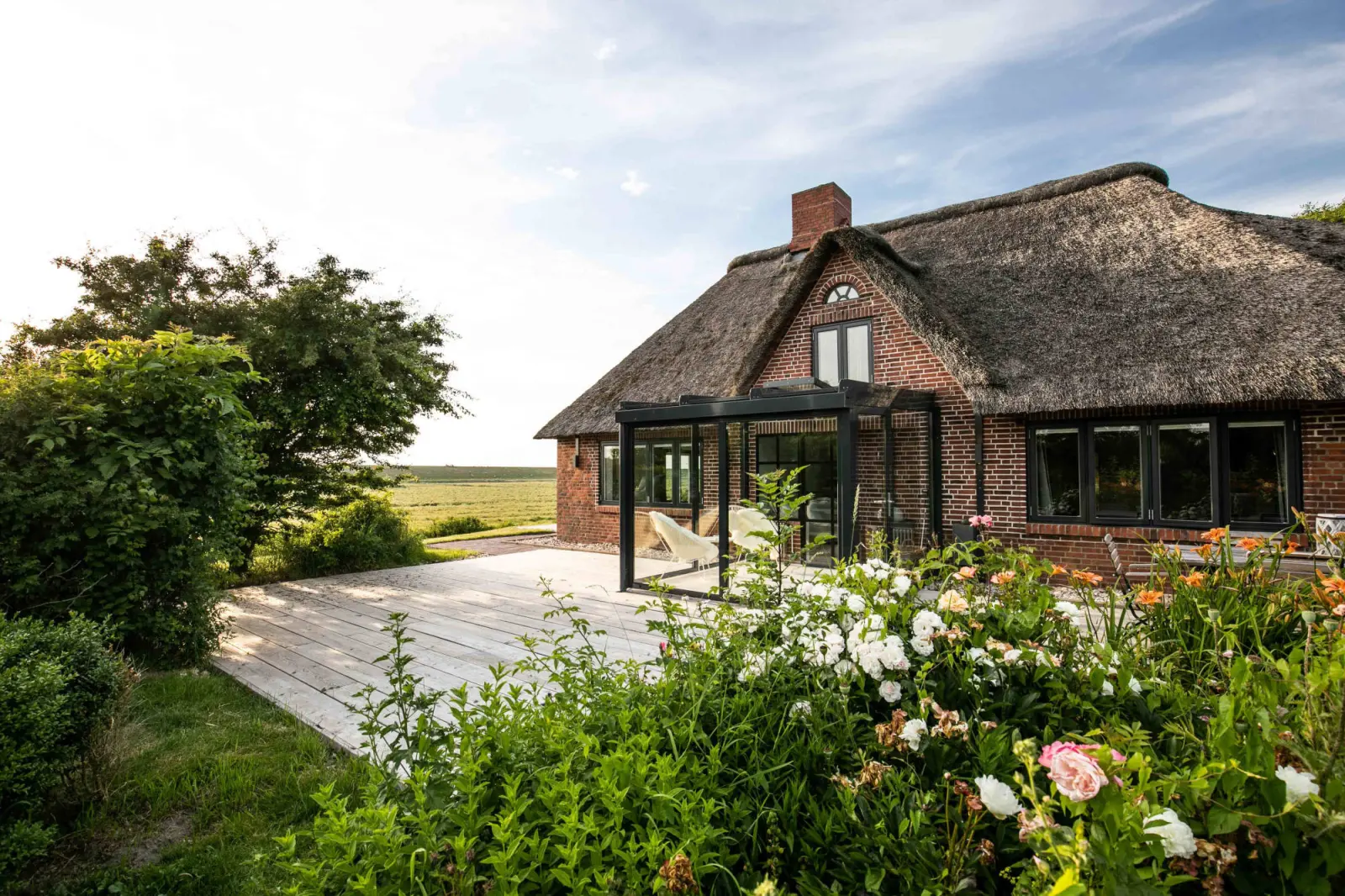 Rückseite des Landhauses mit weitläufiger Holzterrasse, Rosen und Wiesenblick