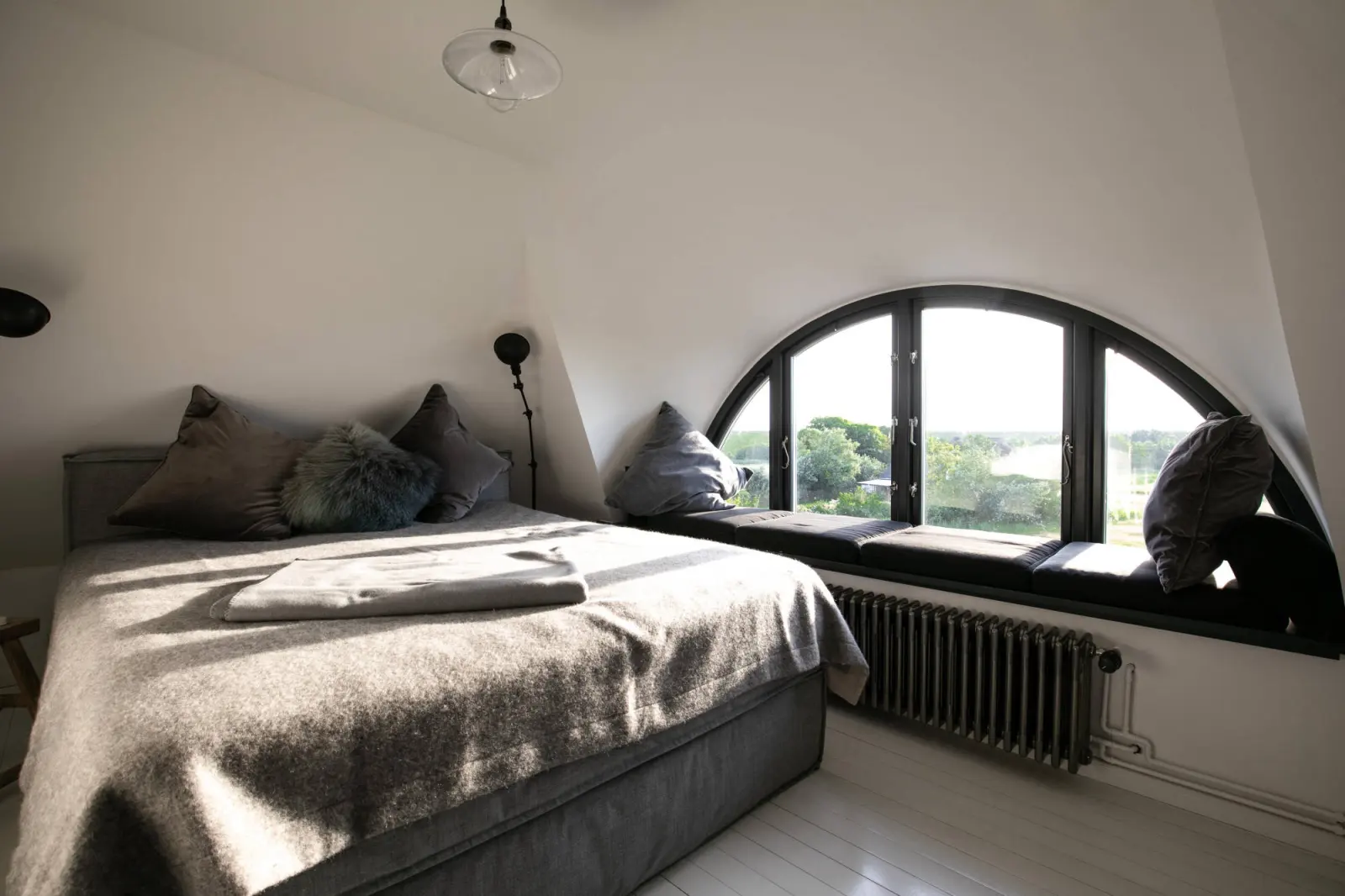 Schlafzimmer mit Boxspringbett, Halbrundfenster mit Sitzbank und Blick in die Marsch