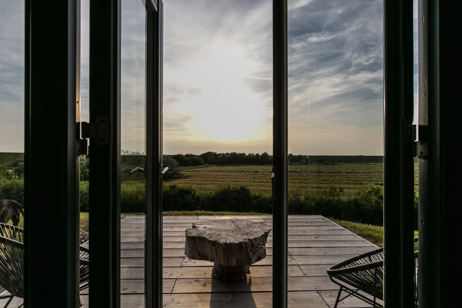 Blick durch offene Terrassentüren auf Holzterrasse und Wiesen im Abendlicht