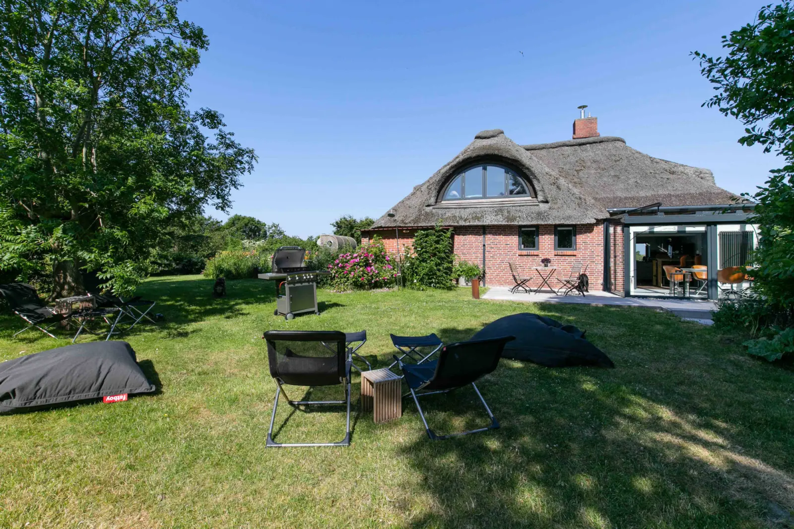 Garten mit Rasen, Sitzsäcken und Klappstühlen vor dem Reetdachhaus