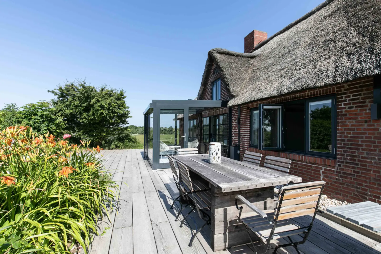 Lange Holzterrasse mit Esstisch und Klappstühlen an der Backsteinfassade