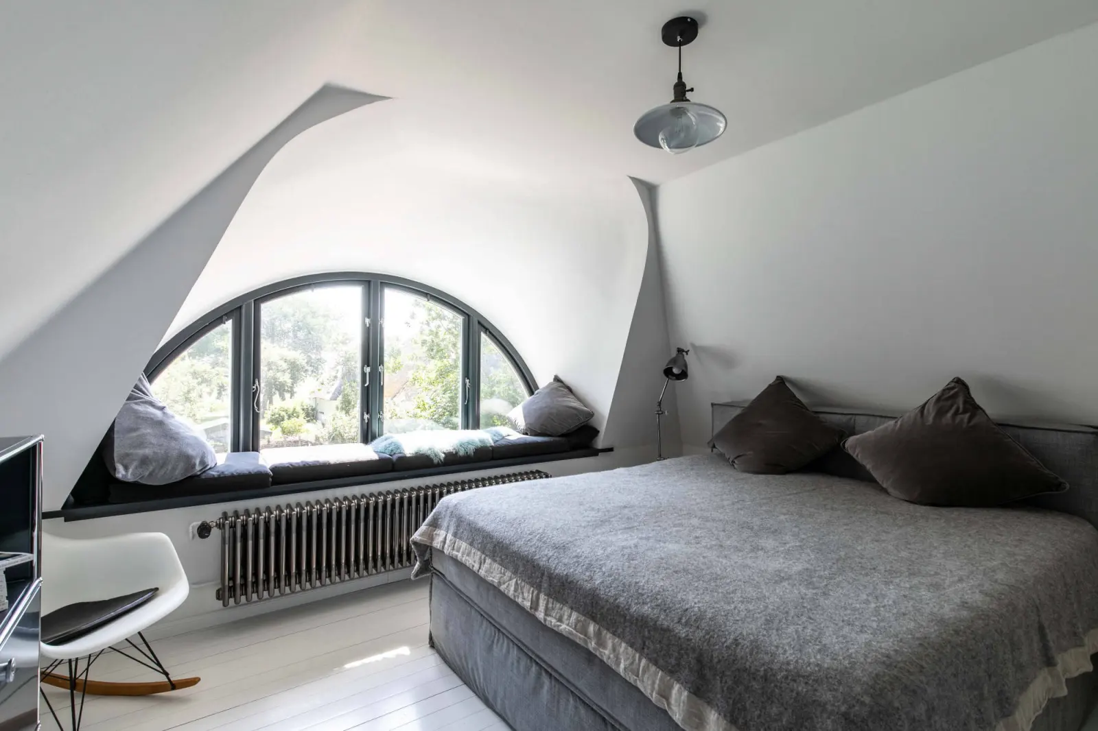 Schlafzimmer unterm Dach mit Halbrundfenster, Sitzbank, Heizkörper und Schaukelstuhl