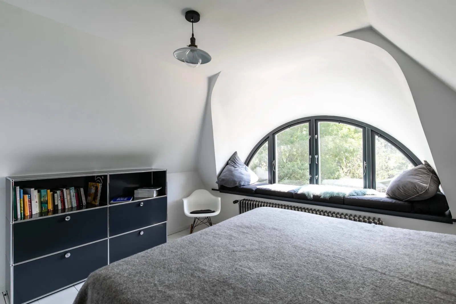 Zimmer mit Halbrundfenster, schwarzem Regal, Bett und Fensterbank mit Kissen