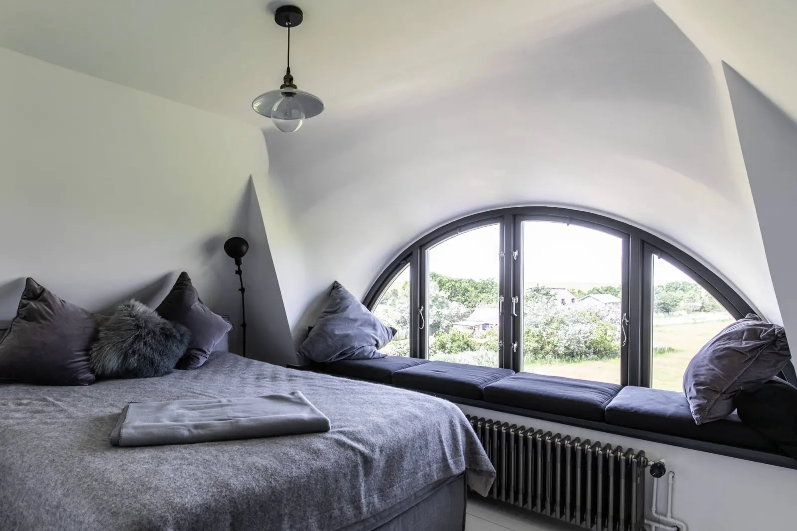 Doppelbett vor dem Halbrundfenster mit gepolsterter Fensterbank und Heizkörper
