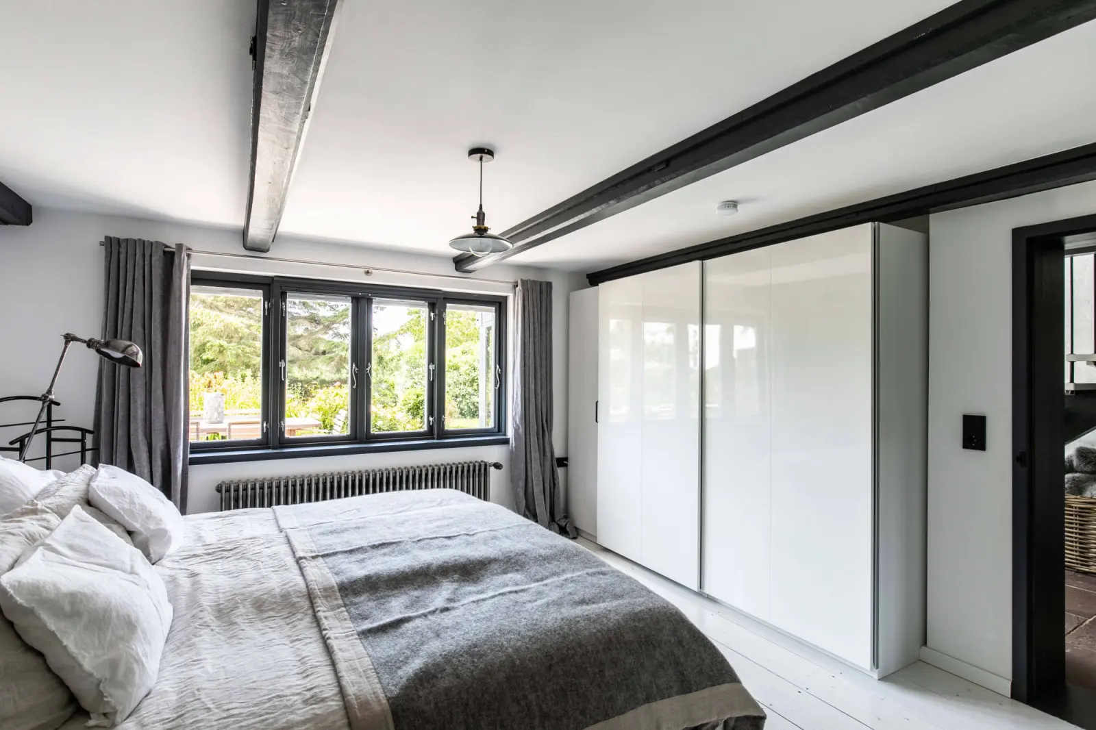 Schlafzimmer mit großem weißem Schiebeschrank und Doppelbett unter Deckenbalken