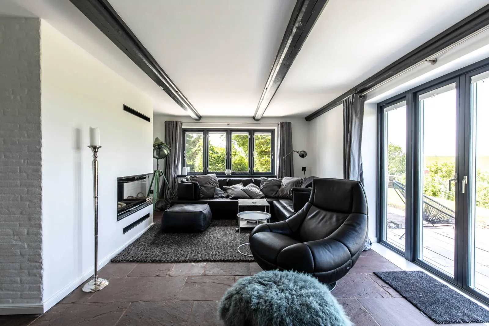 Wohnbereich mit Sofalandschaft, schwarzem Ledersessel und Kamin hinter Glas