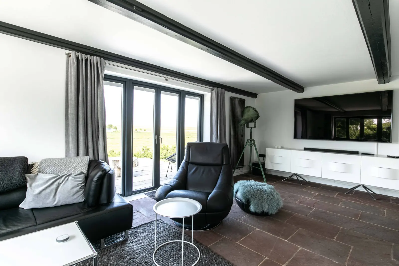 Wohnzimmer mit Ledersessel, TV-Board, Terrassentüren und dunklem Steinboden
