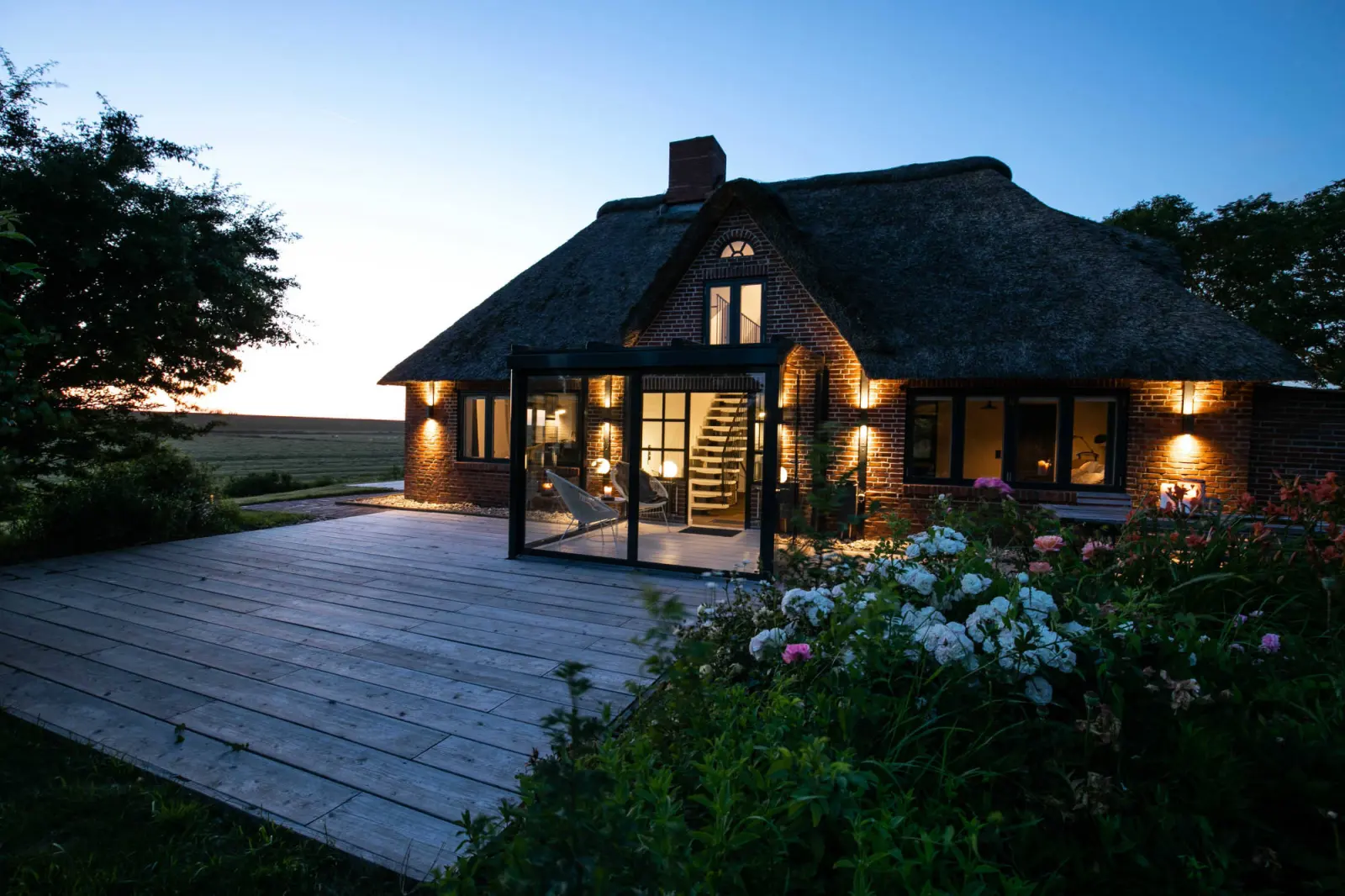 Abendstimmung am Landhaus mit beleuchtetem Wintergarten und Holzterrasse