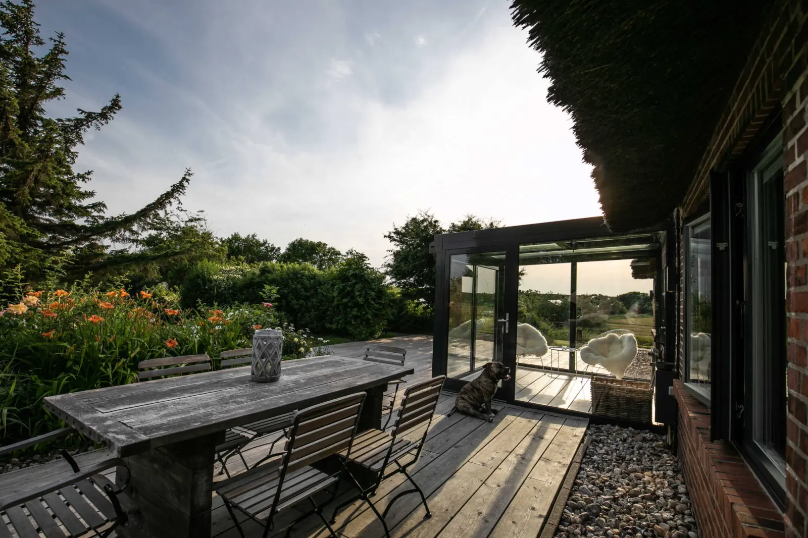 Terrasse mit Holztisch, Klappstühlen und gläsernem Wintergarten am Backsteinhaus
